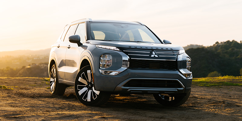 Silver Mitsubishi Outlander parked on a hillside with a scenic sunset background.
