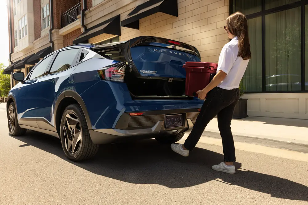 Women holder a box using her foot to open the trunk of a blue 2027 Eclipse Sportback EV